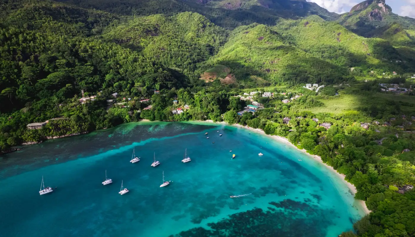 Vue aérienne de la baie de Beau Vallon à Mahé, voiliers au mouillage sur un lagon turquoise devant des collines vertes
