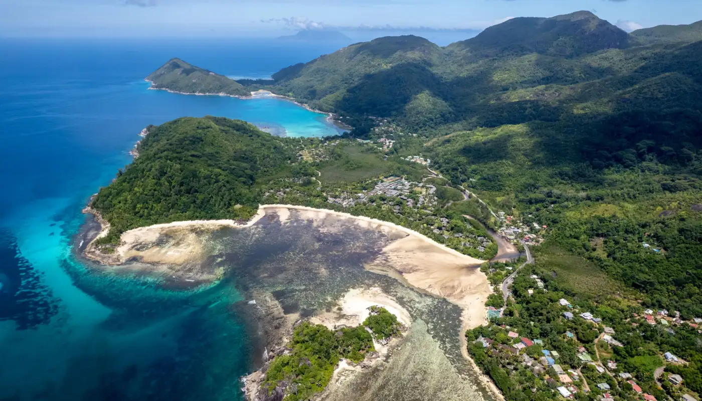 Vue aérienne de la côte de Mahé aux Seychelles, collines boisées, village en bord de mer et lagon turquoise