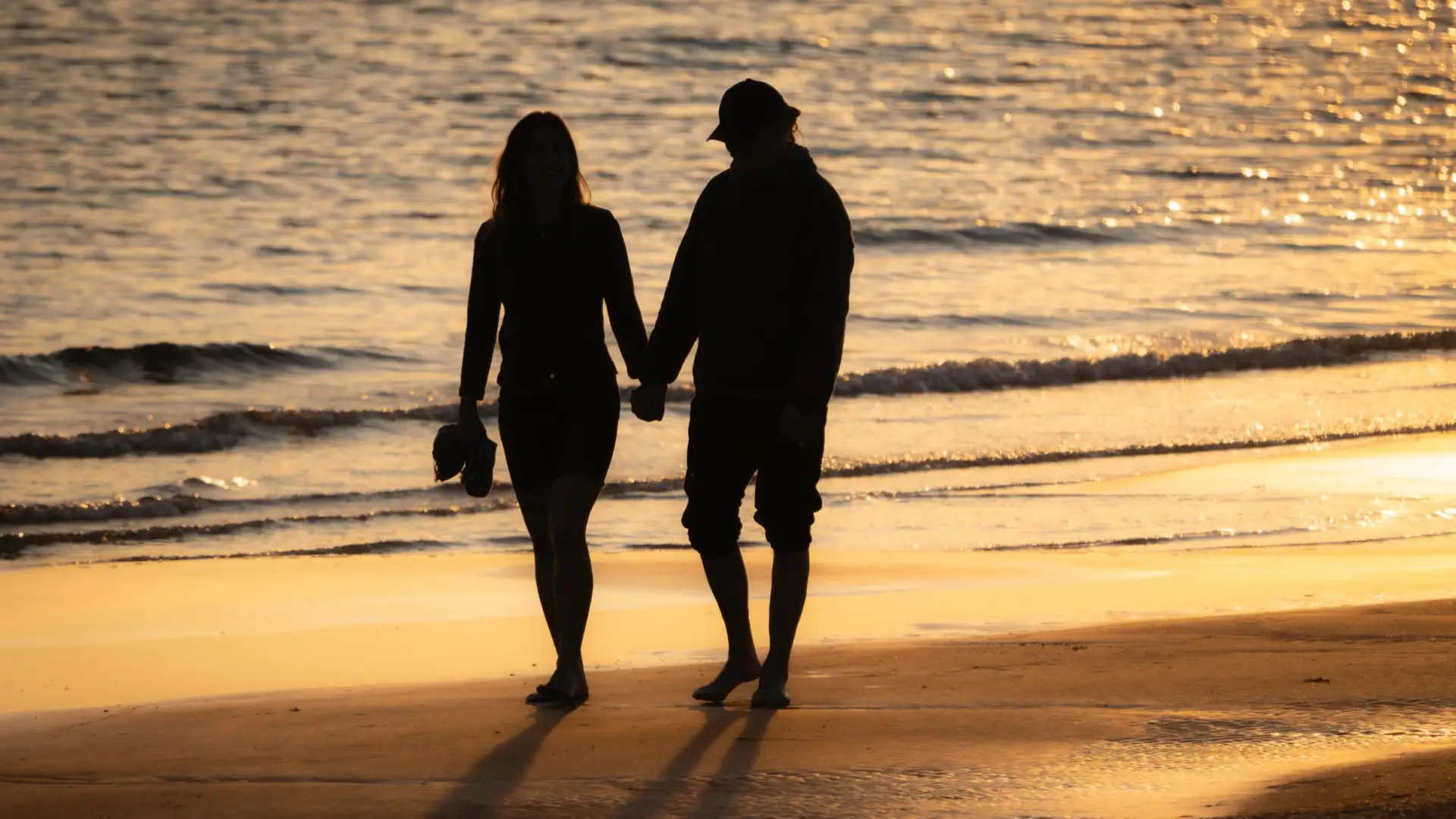 Silhouette d'un couple marchant main dans la main sur une plage au coucher du soleil