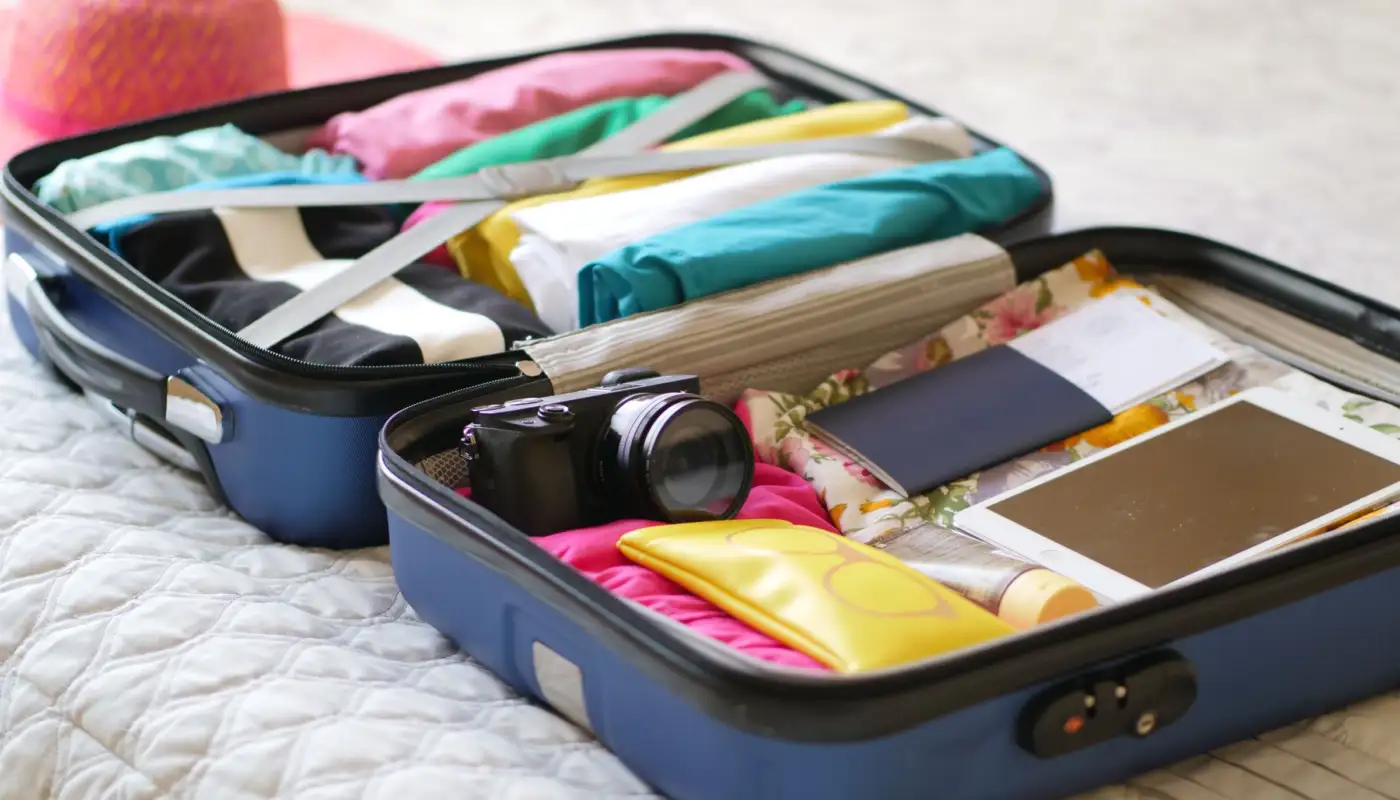 Valise ouverte avec des vêtements pliés, un appareil photo et un passeport, vue de dessus