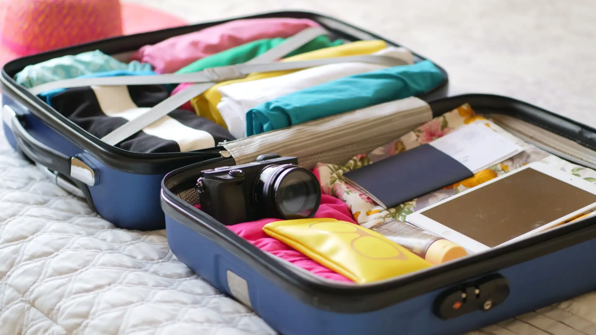 Valise ouverte avec des vêtements pliés, un appareil photo et un passeport, vue de dessus