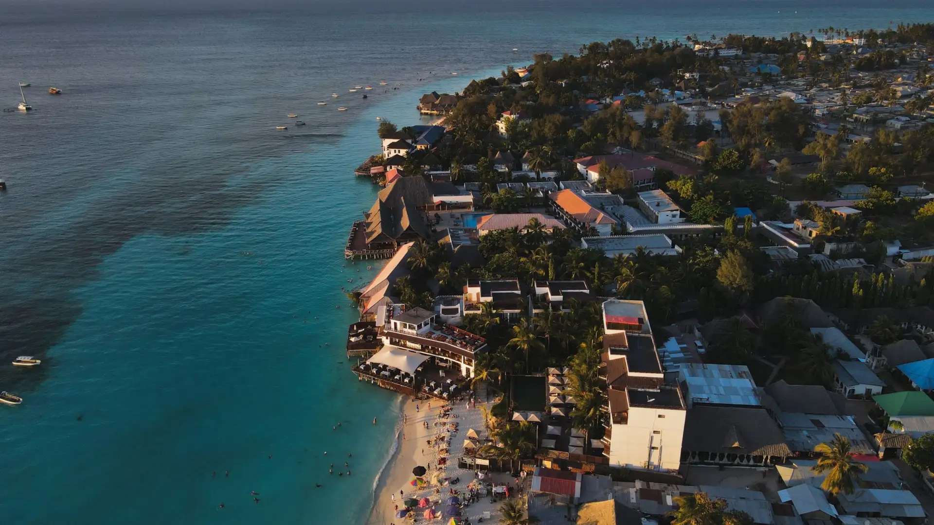 Vue aérienne de la plage de Nungwi au coucher du soleil, hôtels en bord de mer et eau turquoise, pointe nord de Zanzibar