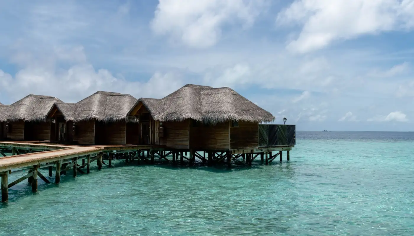 Villas sur pilotis à toit de chaume alignées sur un lagon turquoise aux Maldives