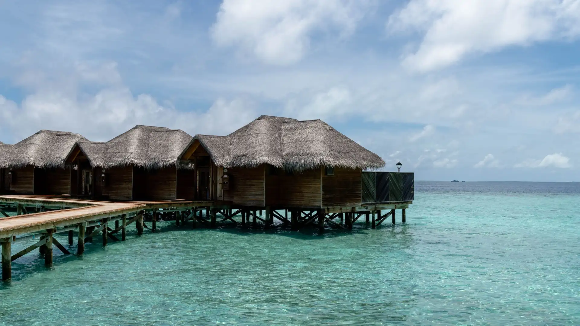 Villas sur pilotis à toit de chaume alignées sur un lagon turquoise aux Maldives